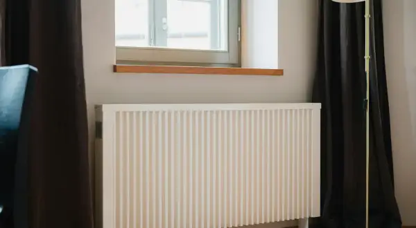 Vitt element med ribbad front, perfekt för att bygga elementskydd. En golvlampa står bredvid.