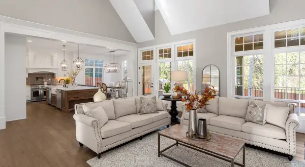 Stilvolles wohnzimmer einrichten mit beigen Sofas, Holzboden und offener Küche. Ein moderner Teppich und ein Couchtisch runden das Bild ab.