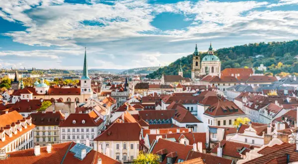 Dachlandschaft von Mala Strana in Prag mit roten Ziegeldächern und Kirchtürmen unter einem blauen Himmel mit Wolken.