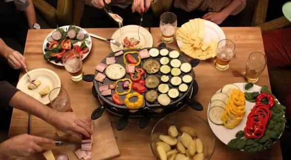 Mesa con raclette, quesos, patatas, ensalada y muchas verduras para raclette: pimientos, calabacín, berenjena y tomate.