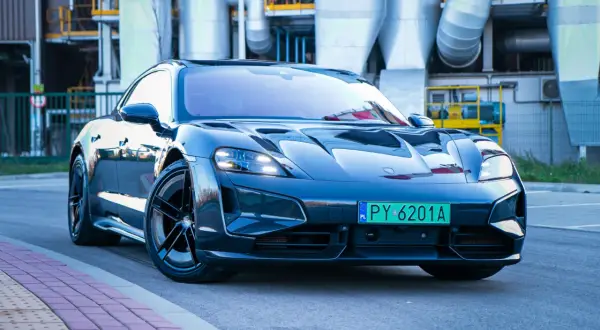 Elegancki Porsche Taycan Turbo S błyszczy na tle przemysłowej architektury.