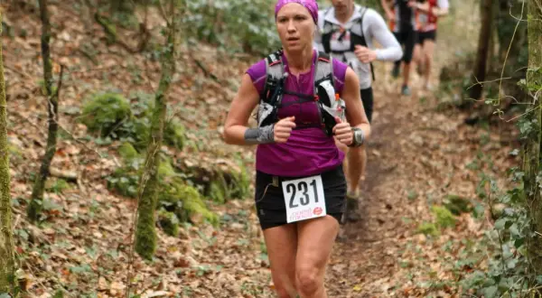 Une coureuse, dossard 231, s'élance sur un trail débutant en forêt. D'autres coureurs la suivent.