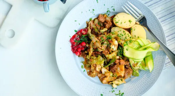 En tallrik med stuvad vitkål, köttfärs, kokt potatis, gurkband och rårörda lingon. Ett härligt kålmaja recept för en smakrik middag.