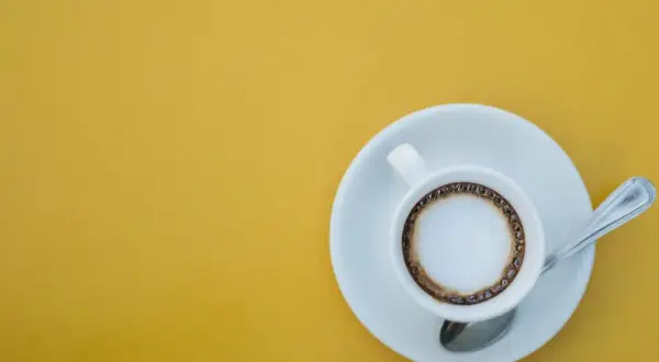 En vit kopp med kaffe macchiato står på en tefat med en sked. En perfekt start på dagen, det är vad macchiato betyder.