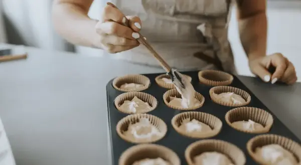 En person fyller muffinsformar med smet. Bra baka tips för perfekta muffins.