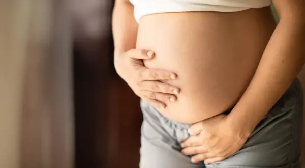 Brzuch kobiety w ciąży, która odczuwa częste oddawanie moczu w ciąży 1 trymestr. Dłonie obejmują zaokrąglony brzuch.