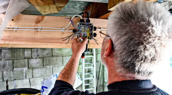 Elektryk kończy instalację elektryczną w garażu, łącząc przewody w puszce.
