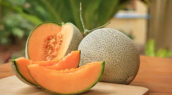 Melón entero y cortado, mostrando su pulpa naranja y semillas. Un festín de las propiedades del melón.