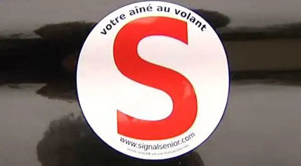Macaron "votre aîné au volant" sur une voiture. Le S rouge est bien visible.