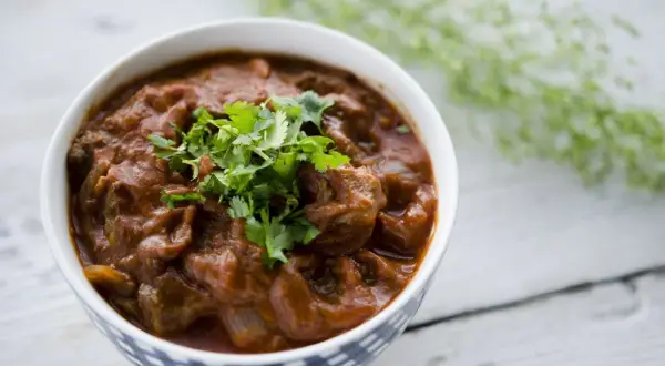 Miseczka z gęstym, pomarańczowym gulaszem tikka masala, ozdobiona świeżą kolendrą.