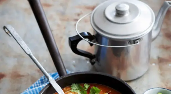 Gęste, aromatyczne gumbo z krewetkami i kiełbasą, gotowe do podania. Obok metalowy czajniczek i ćwiartki limonki.