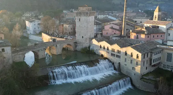 Cascata e ponte ad arco a Fermignano, vicino Urbino, con edifici storici e una ciminiera.