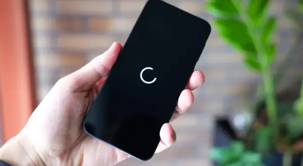 Dłoń trzyma czarny smartfon z białym kółkiem ładowania na ekranie.