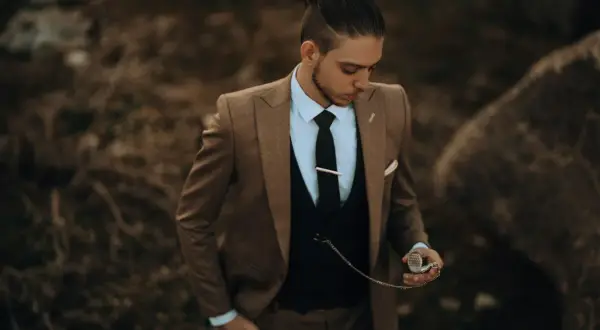 Stilberatung für Senioren: Mode ab 60. Ein Mann im eleganten braunen Anzug mit Weste und Krawatte hält eine Taschenuhr.