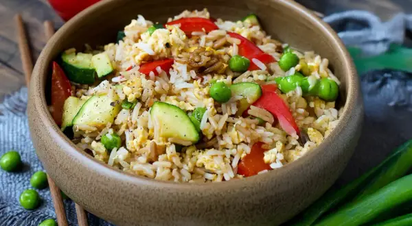 Schüssel mit gebratenem Reis, Erbsen, Zucchini und Paprika. Ein köstliches Gericht mit Reis, das zum Genießen einlädt.