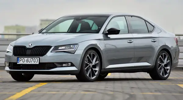 Elegancki, szary Skoda Superb 2024 z czarnym dachem i przyciemnianymi szybami, zaparkowany na parkingu.