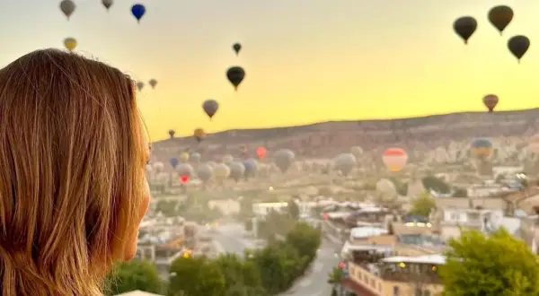 Kvinna ser på en magisk soluppgång över Kappadokien, Turkiet, med hundratals luftballonger som svävar i den gyllene himlen.