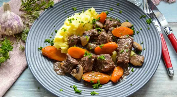 Herzhaftes Boeuf Bourguignon Rezept: zartes Rindfleisch mit Karotten, Pilzen und Kartoffelpüree auf einem grauen Teller, garniert mit Petersilie.