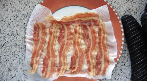 Fertig gegrillter Bacon auf Küchenpapier auf einem Teller. Schnell und einfach in der Mikrowelle zubereitet.
