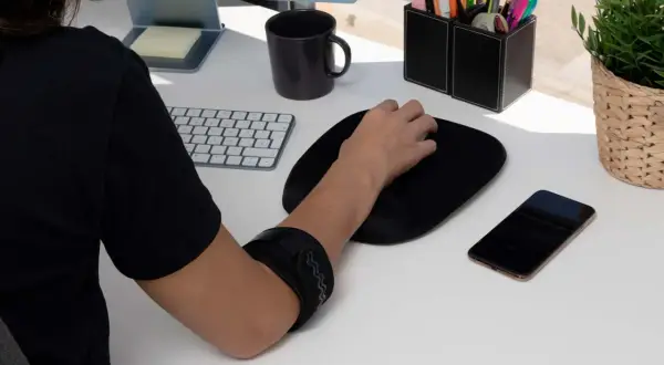 Braccio con tutore per alleviare il dolore mano mouse. Tastiera, mouse, telefono e pianta sul tavolo.