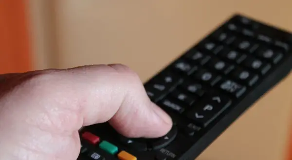 Dłoń naciska przycisk na pilocie, by dowiedzieć się, jak odbierać wszystkie kanały telewizji naziemnej.