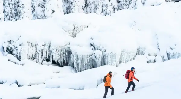Två personer med ryggsäckar vandrar på vintern i ett snöigt landskap med istappar.
