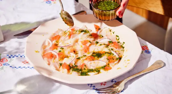 Préparation d'un carpaccio de bar frais avec pamplemousse, oignon rouge et une vinaigrette aux herbes.