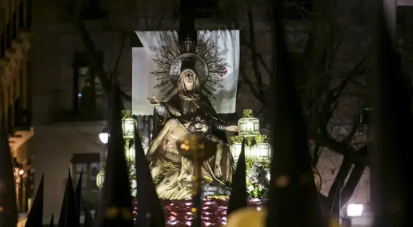 Procesión de Jueves Santo Zaragoza: imagen de la Virgen con el cuerpo de Cristo, rodeada de faroles y capirotes.