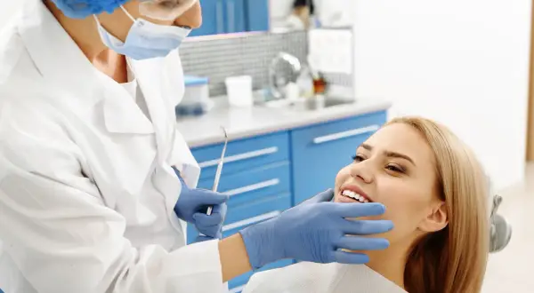 Dentystka bada uśmiechniętą pacjentkę, by wykluczyć zapalenie okostnej i ropień zęba.