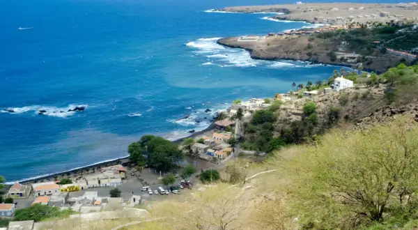 Vue d'un village côtier au Cap-Vert, avec des maisons blanches et colorées nichées sur une colline. Le nom de famille cap verdien résonne dans l'air salin.