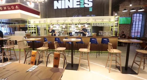 Wnętrze restauracji Lewandowskiego "NINE9S" z barem, stołkami i stołami.