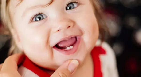 Ein Baby lächelt stolz und zeigt seinen ersten Zahn.