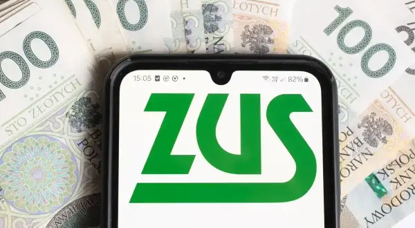 Telefon z logo ZUS na tle banknotów 100 zł. Czas na opłacenie składek ZUS.