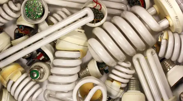 Stos zużytych żarówek energooszczędnych, w tym spiralnych i prostych jarzeniówek, z widocznymi elementami elektronicznymi.