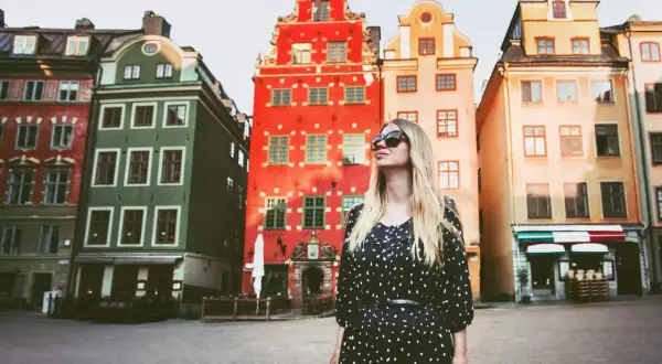 En kvinna med solglasögon står framför färgglada hus på ett torg. Kanske är detta sveriges vackraste stad.