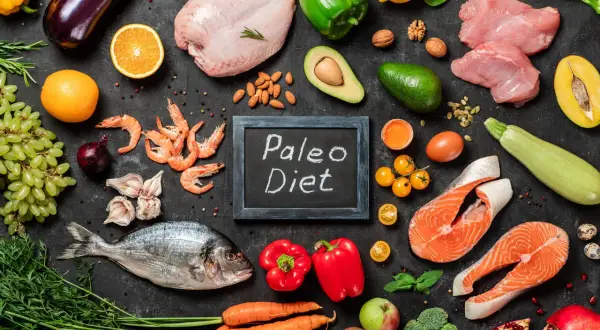 Na czarnej tablicy napis "Paleo Diet". Wokół świeże ryby, mięso, owoce, warzywa i orzechy – składniki diety paleo.
