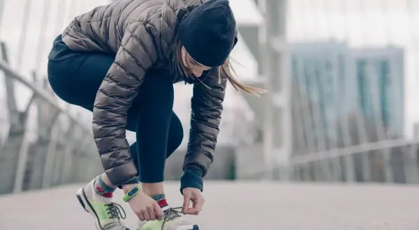 Une femme en tenue de running hiver attache ses lacets sur un pont.