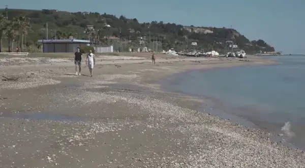 Passeggiata sulla spiaggia di Marina di Campofilone, con due uomini che camminano e barche ormeggiate sullo sfondo.