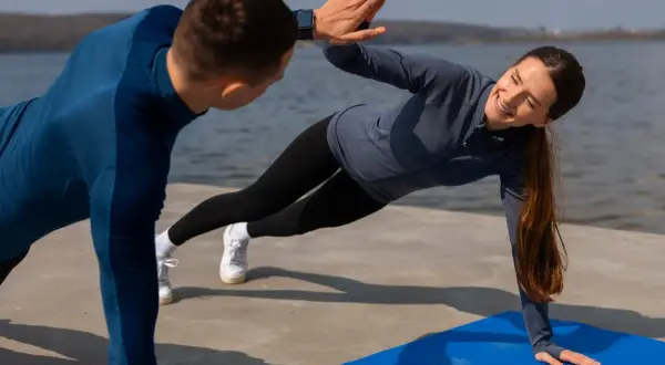 Para ćwiczy na macie nad wodą, wykonując boczne deski i dając sobie high five. Idealny sport dla par.
