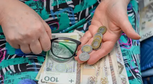 Dłonie trzymają okulary i garść monet na tle polskich banknotów. Zastanawiasz się, ile wynosi renta częściowo niezdolny do pracy?