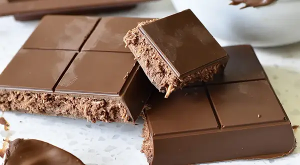 En fransk chokladtårta med krispigt fyllning, uppdelad i bitar. En sked med chokladkräm syns i förgrunden.