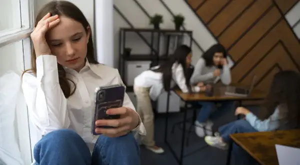 Dziewczyna z telefonem, zmartwiona, w tle inne osoby. Czy to początek problemów z kleptomanią?