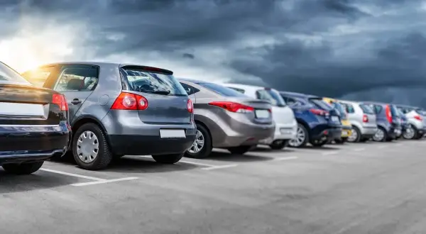 Rząd samochodów na parkingu, w tym jeden z włoską rejestracją, pod burzowym niebem.