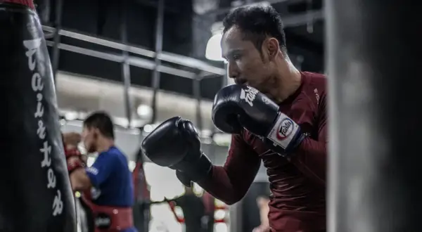 A boxer, sweating and focused, throws a powerful southpaw jab at a heavy bag in a dimly lit gym.