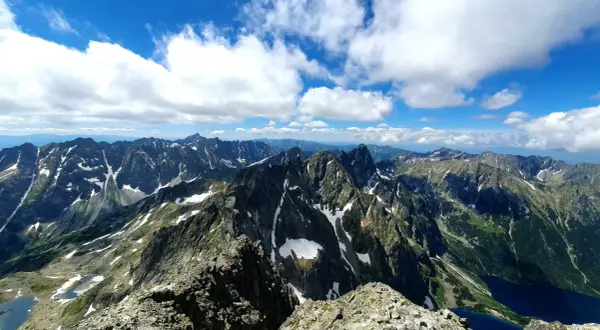 Widok na pasmo górskie Rysy, gdzie szlak wije się wśród skalistych zboczy i resztek śniegu.