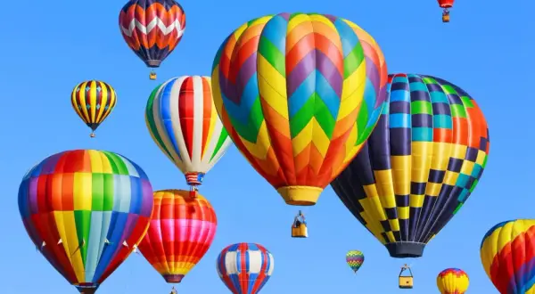 Wiele kolorowych balonów na gorące powietrze unosi się na błękitnym niebie.