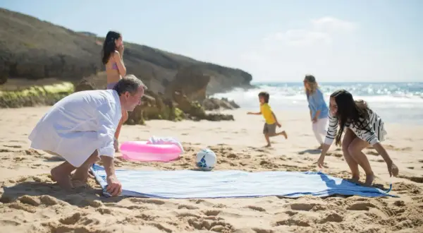 Rodzina cieszy się urlopem nad morzem. Dzieci biegają po plaży, a rodzice rozkładają ręcznik.