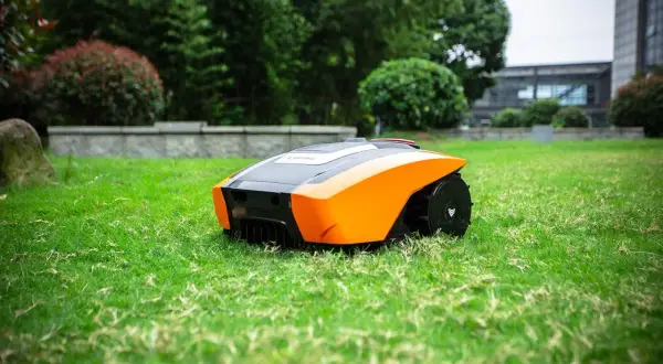 Robot cortacésped autónomo de color naranja y negro, listo para mantener impecable el césped artificial de un jardín moderno.