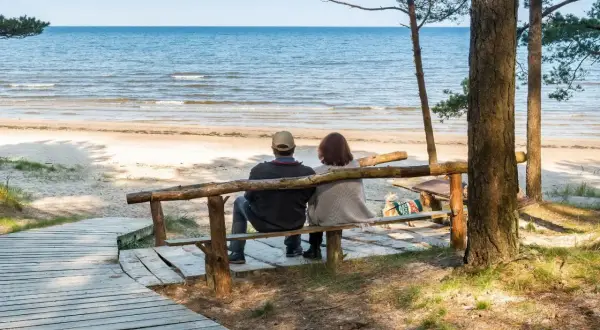 Para relaksująca para siedzi na ławce, patrząc na morze. Idealne miejsce na sanatoria nad morzem.