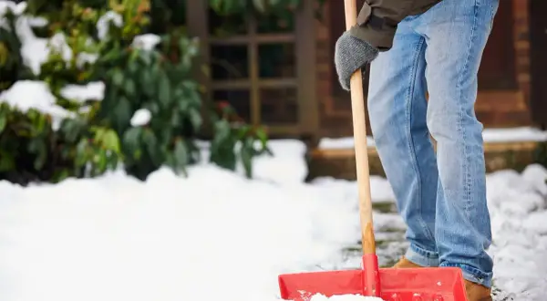 Mann schaufelt Schnee, um dem Winterdienst-Gesetz nachzukommen.